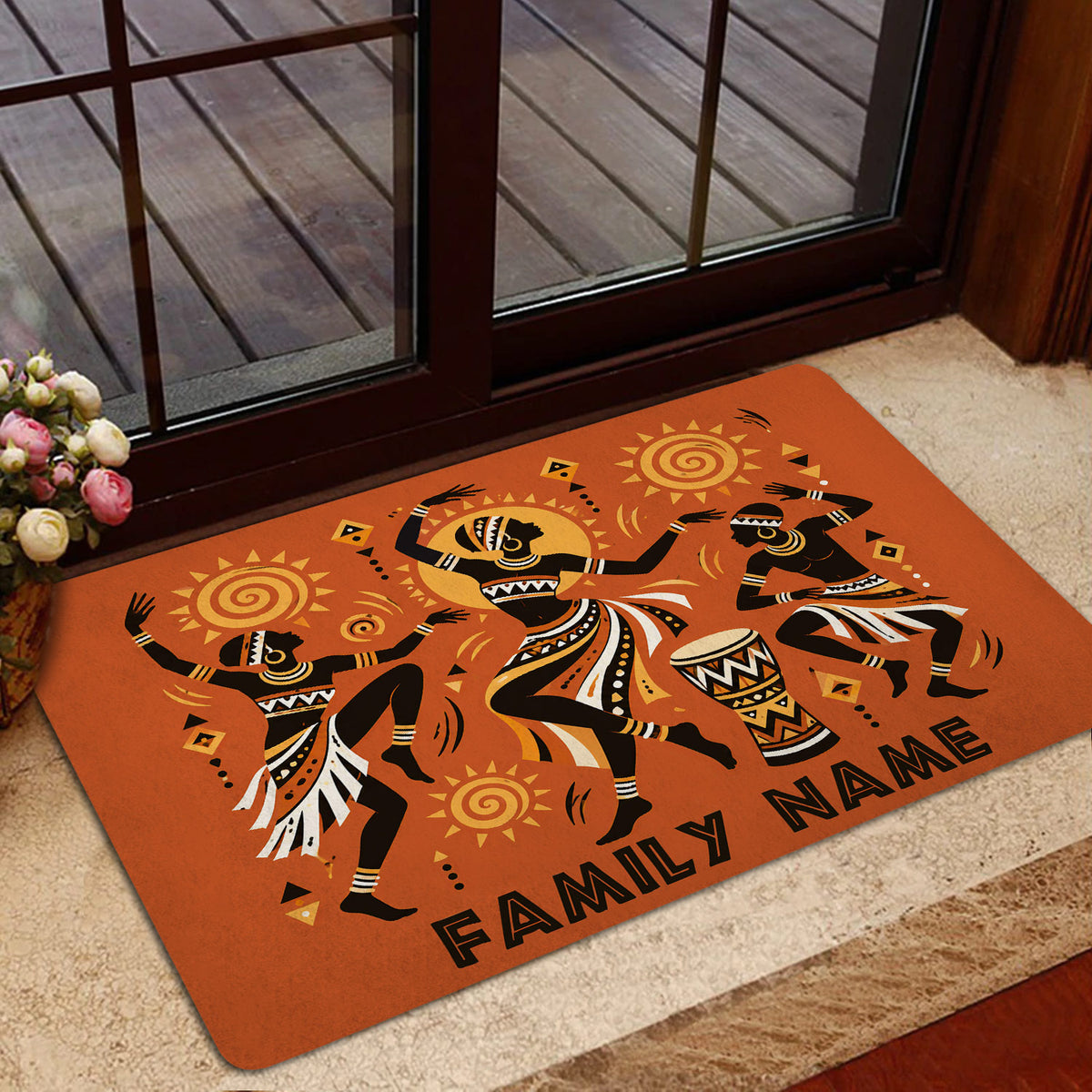Orange African dance doormat styled inside a glass doorway with a neutral floor and floral arrangement