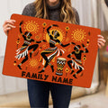Person holding an orange African-inspired doormat featuring dancers, sun symbols, geometric details, and a drum