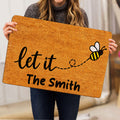 Person holding a golden bee doormat featuring a flying honeybee and welcoming artwork