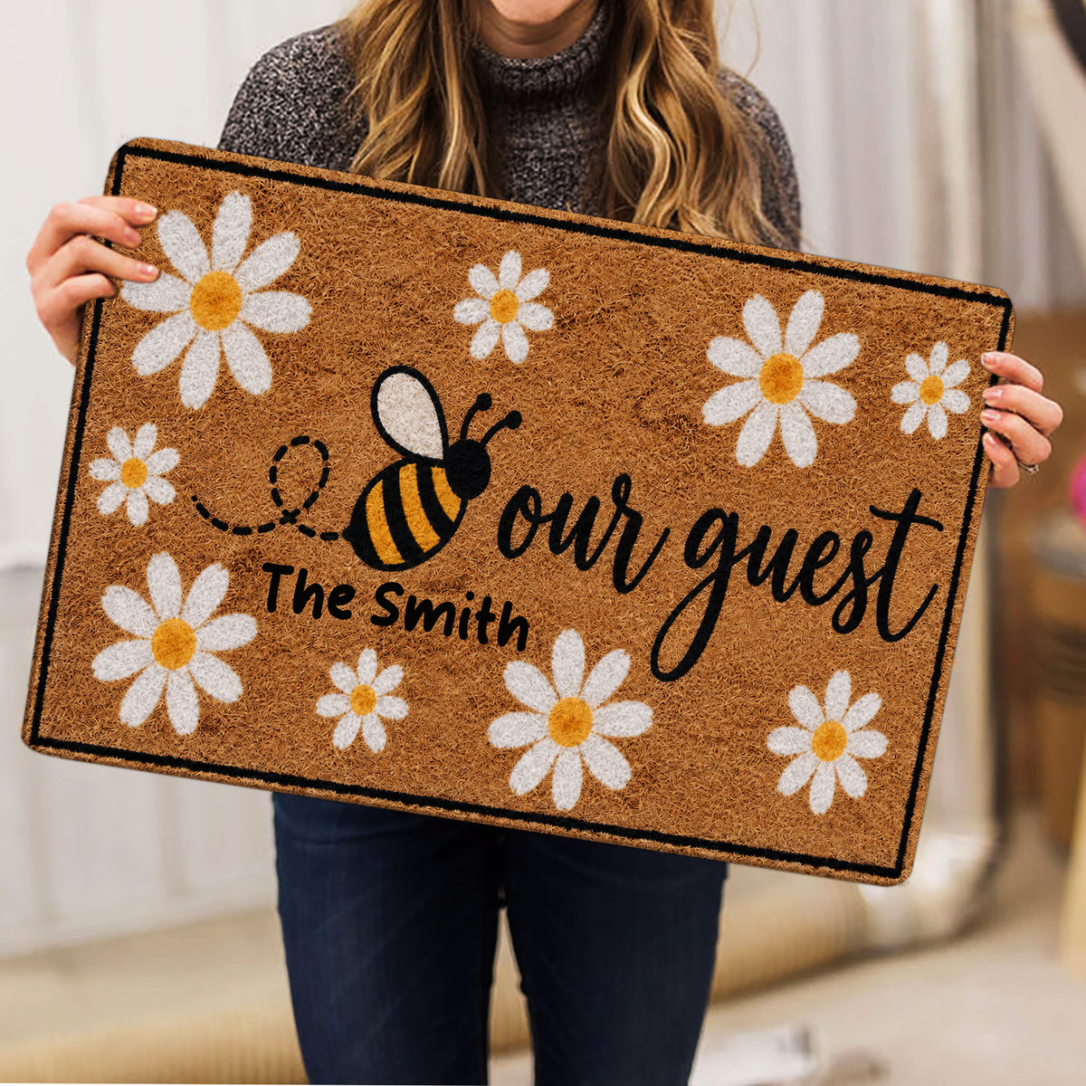 Person holding a bee and daisy doormat featuring a warm floral welcome design
