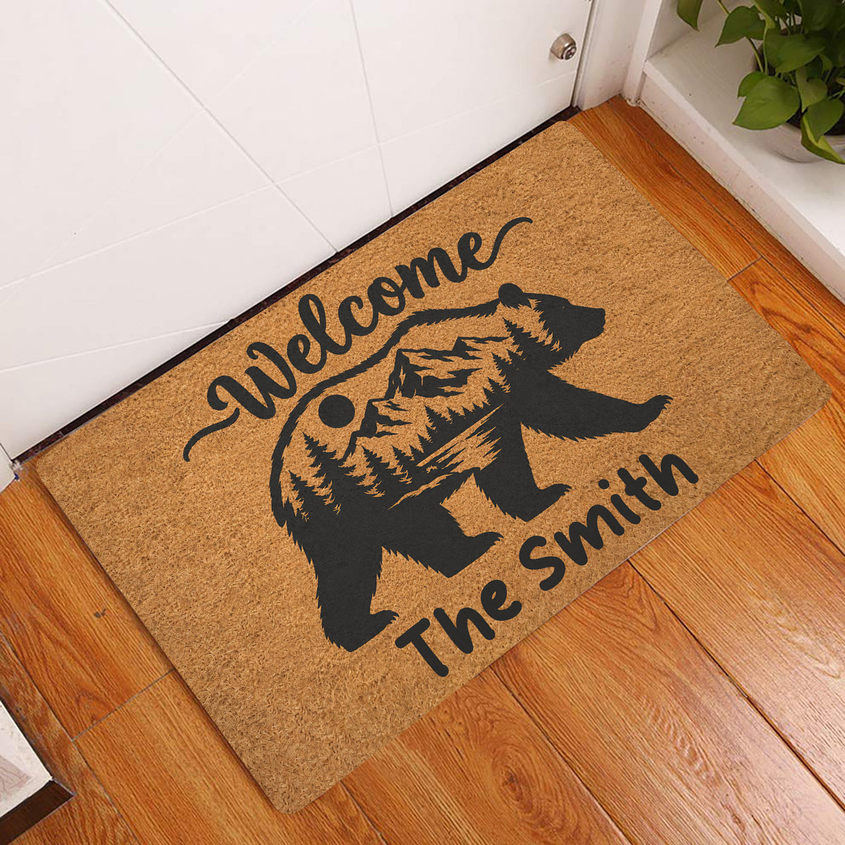 Bear welcome doormat displayed in an indoor entryway on a warm wood floor beside a white door