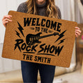 Person holding a rock and roll doormat featuring an electric guitar and bold black lettering