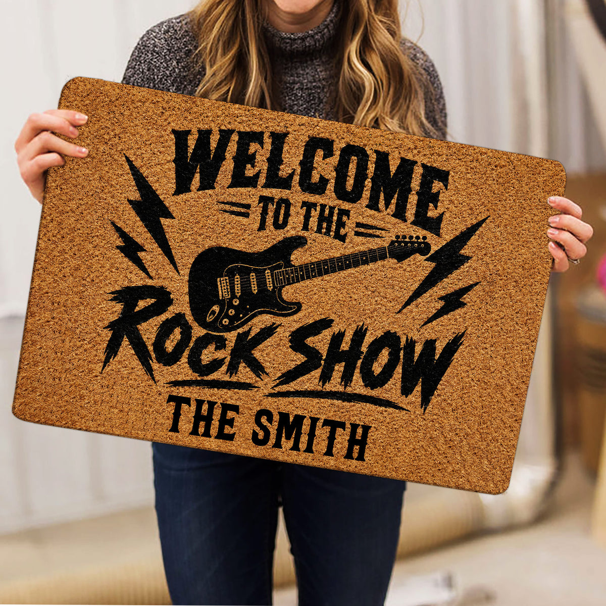 Person holding a rock and roll doormat featuring an electric guitar and bold black lettering