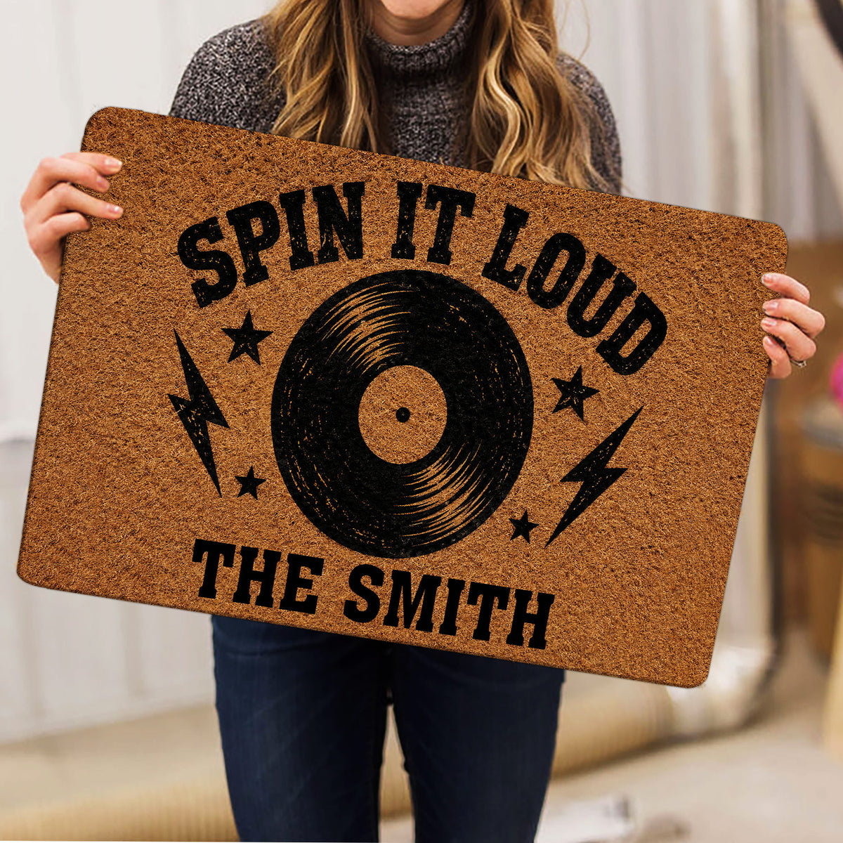 Person holding a rock and roll doormat featuring a black vinyl record and bold music-inspired artwork