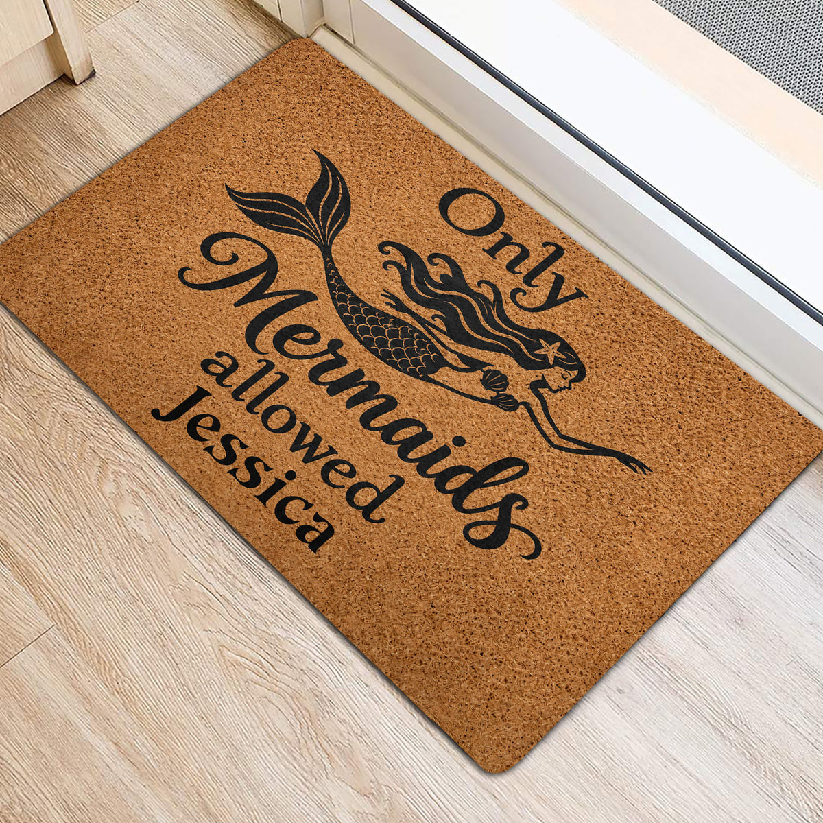 Mermaid door mat positioned near a doorway, featuring a black mermaid illustration and lettering