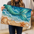 Mermaid doormat held indoors, showing a colorful ocean beach scene with a detailed turquoise tail