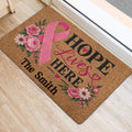 Pink ribbon breast cancer door mat displayed at an indoor entrance with floral artwork