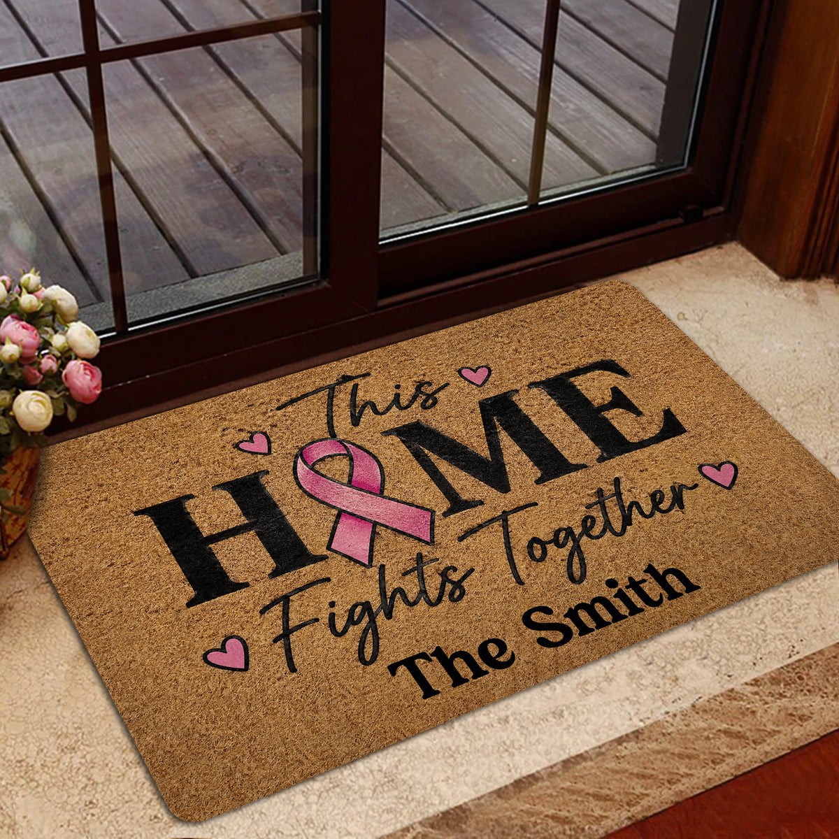 Breast cancer support doormat presented near a glass entry door with flowers nearby