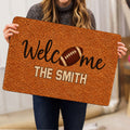 Football doormat shown in a lifestyle presentation with a brown football design and welcome message