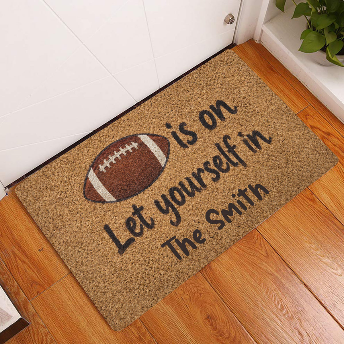 Football entryway doormat displayed beside a white door on a warm wood floor