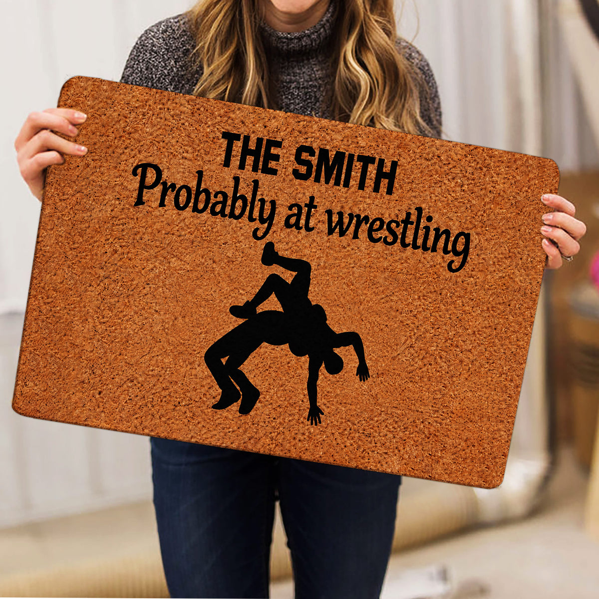 Person holding a wrestling-themed doormat featuring a bold black grappling silhouette