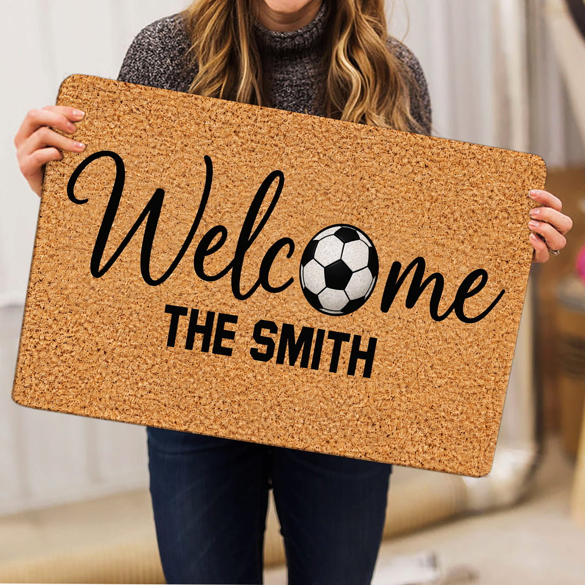 Soccer doormat held indoors, showing the welcome artwork and black-and-white soccer ball design