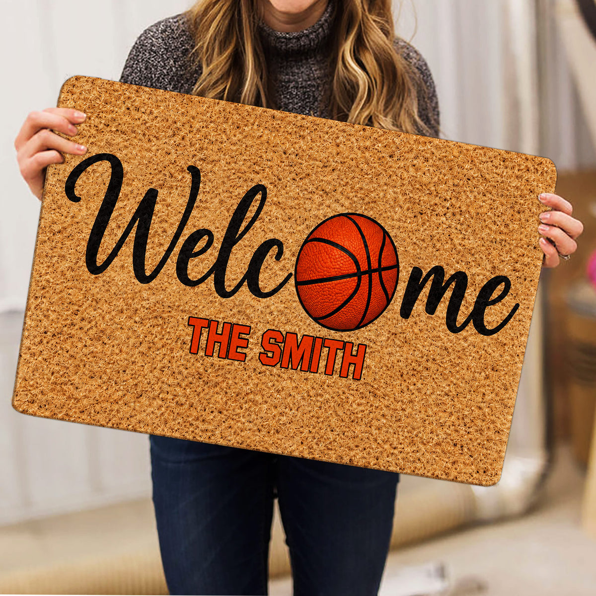 Person holding a basketball welcome doormat featuring an orange basketball and bold lettering