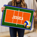 Volleyball doormat held upright to display its green court border, orange playing area, and ball artwork