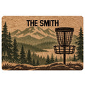 Disc golf doormat featuring a basket, mountain landscape, and evergreen forest artwork