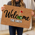 Person holding a golf welcome doormat featuring a putting green and red flag