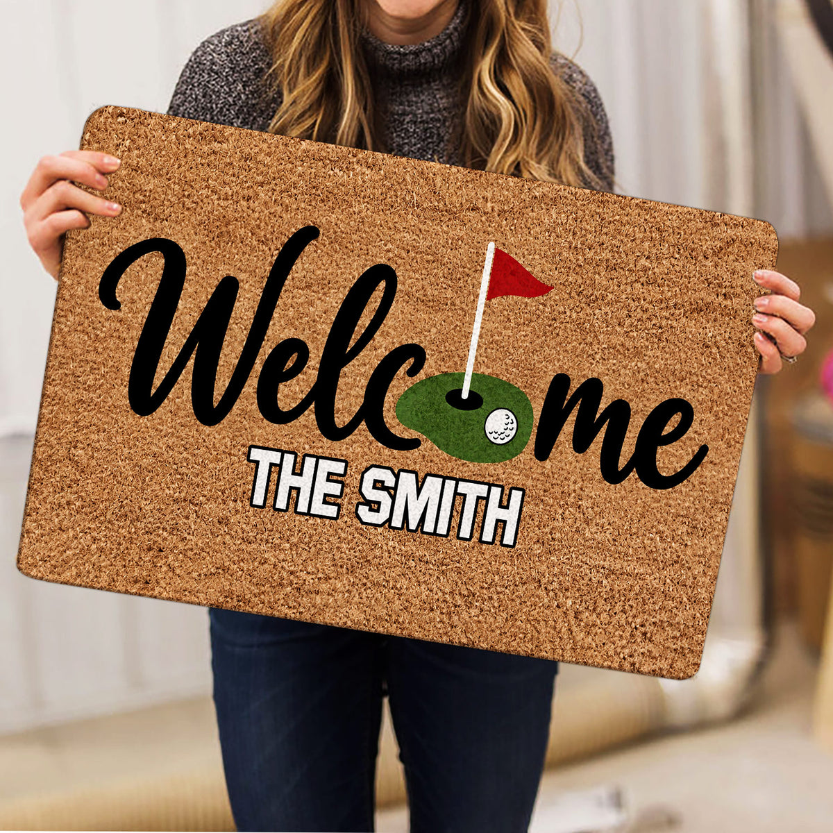 Person holding a golf welcome doormat featuring a putting green and red flag