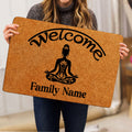Person holding a yoga doormat featuring a meditating figure, lotus motifs, welcome lettering, and family wording