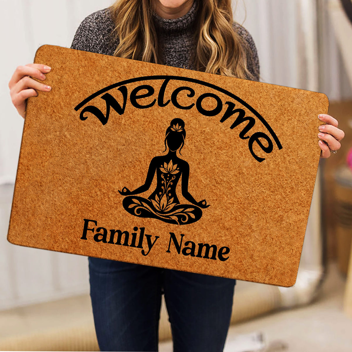 Person holding a yoga doormat featuring a meditating figure, lotus motifs, welcome lettering, and family wording
