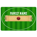 Green cricket doormat featuring a cricket pitch, wickets, ball, and bold family lettering