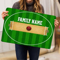 Person holding a green cricket pitch doormat featuring wickets and a cricket ball