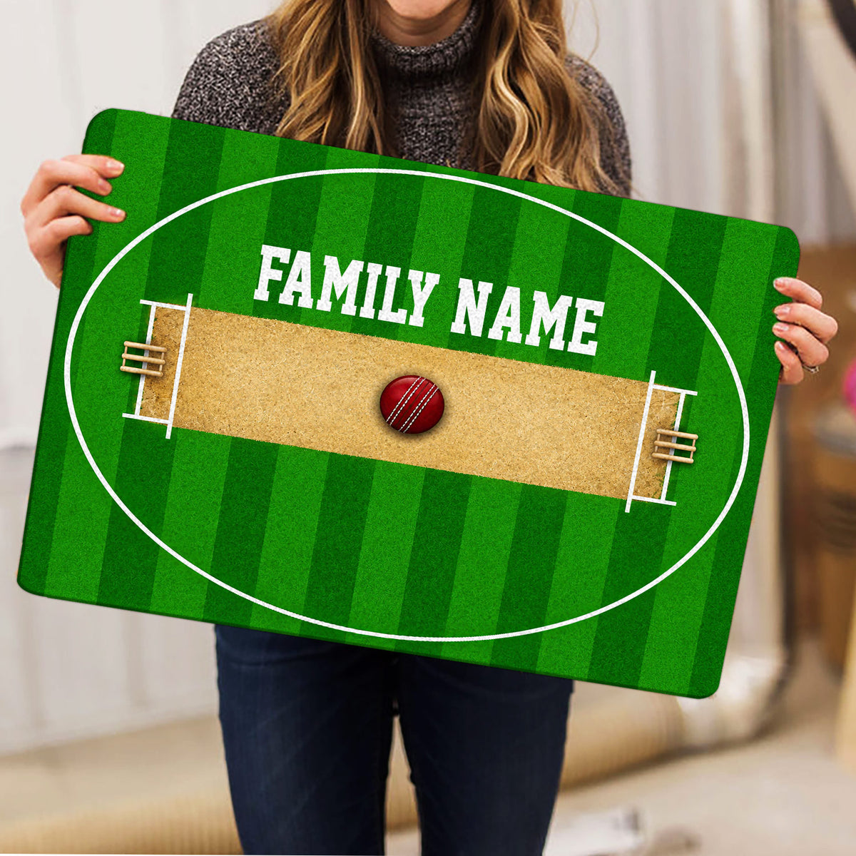 Person holding a green cricket pitch doormat featuring wickets and a cricket ball