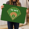 Person holding a green baseball doormat showing a ballpark diamond and striped field artwork