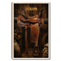 Framed cowboy wall art featuring a detailed brown Western saddle against rustic dark wood