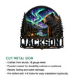 Bear metal sign shown with a dramatic aurora landscape, forest, lake, mountains, and campfire artwork