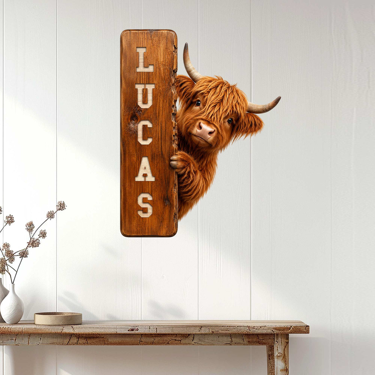 Highland cow metal sign displayed on a white paneled wall above a rustic console table