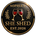 Custom wine metal sign with clinking red wine glasses, gold laurel accents, and a bold she shed design