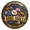 Floral She Shed metal sign with colorful wildflowers, ornate gold banner, and round black-and-gold frame
