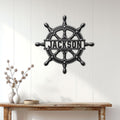 Nautical ship wheel metal sign displayed on a white paneled wall above a console table