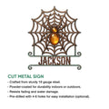 Cut-metal spider sign featuring a detailed web design, jeweled amber body, and curled lower frame
