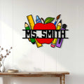 Teacher apple metal sign displayed on a white paneled wall above a wood console table