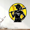 Softball wall decor displayed on a white paneled wall, featuring a female batter silhouette and vivid yellow baseball