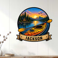 Kayak wall sign displayed on a white paneled wall, featuring a mountain lake, cabin, and colorful sunset