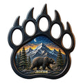 Bear paw-shaped metal sign featuring a walking bear, mountain landscape, pine trees, and moonlit sky