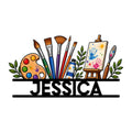 Artist metal sign featuring colorful paintbrushes, palette, easel, paint tubes, and leafy accents