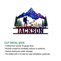 Mountain trekking metal sign shown with a vibrant alpine scene, evergreen trees, trail, and hiker silhouette