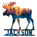 Moose-shaped metal sign featuring a forest lake sunset scene in vibrant orange, purple, and blue tones