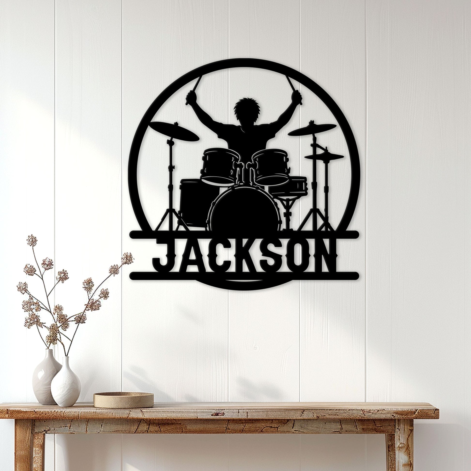 Black drummer metal wall sign displayed on a light paneled wall above a wooden console