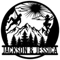 Rock climbing metal sign with two climbers silhouetted against mountains, pine trees, and a rising sun
