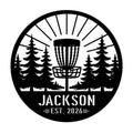 Round disc golf metal sign featuring a basket surrounded by pine trees and a bold forest course silhouette