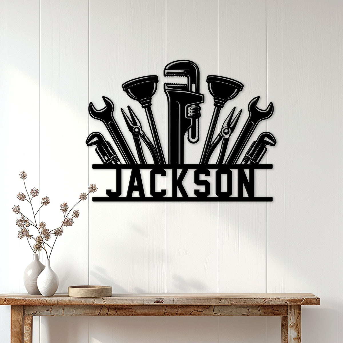 Black plumber tool metal sign displayed on a light paneled wall above a wood console table