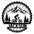 Mountain biking metal sign with a cyclist riding through mountain peaks and evergreen trees inside a tire design