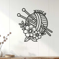 Black knitting wall sign with yarn and needles displayed on a light wood-paneled wall