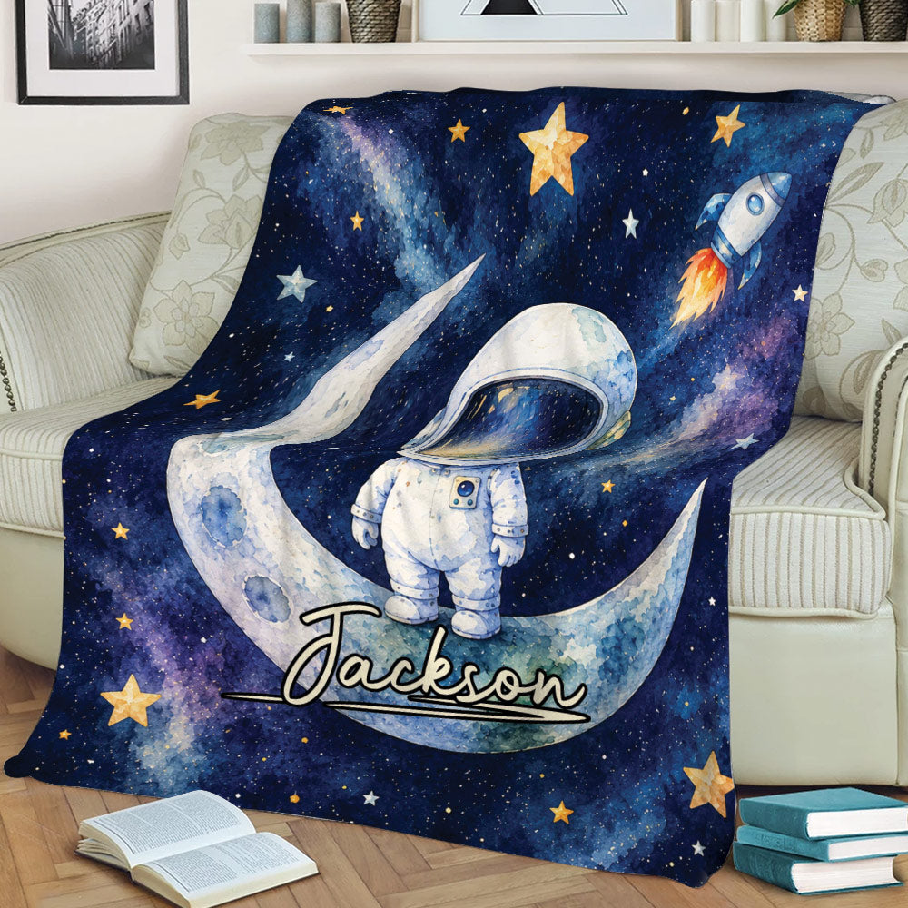 Close view of an astronaut throw blanket with watercolor space, moon, rocket, and star details