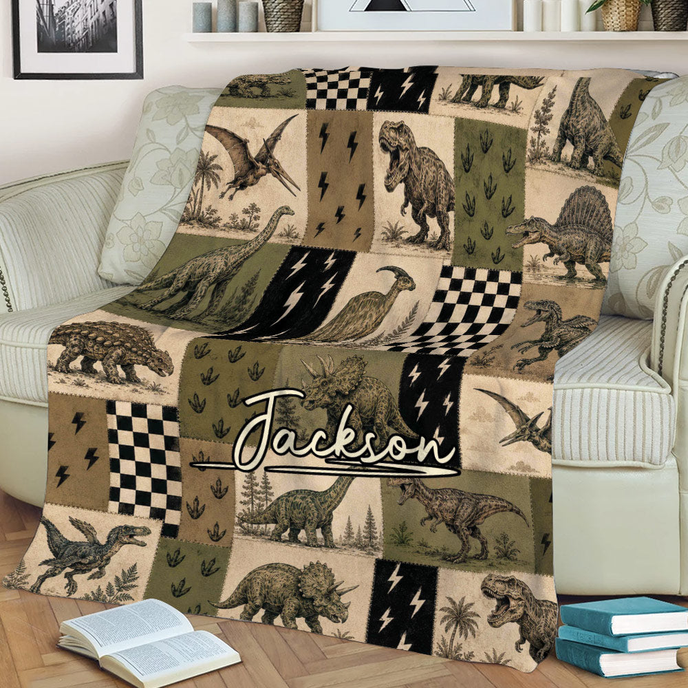 Dinosaur blanket styled across a sofa with illustrated T-rex, triceratops, stegosaurus, and pterosaur artwork