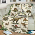 Dinosaur throw blanket draped over a couch, featuring detailed dinosaur illustrations and tropical botanical accents